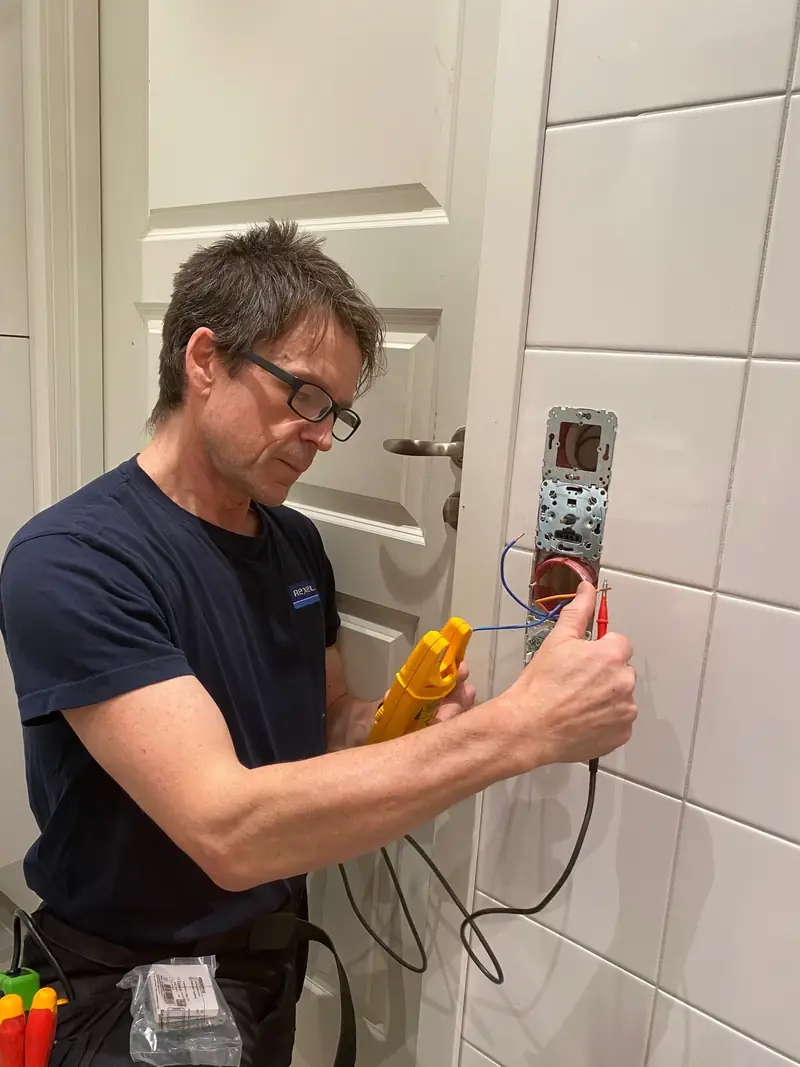 Elektriker mäter vid ett vägguttag under en elbesiktning